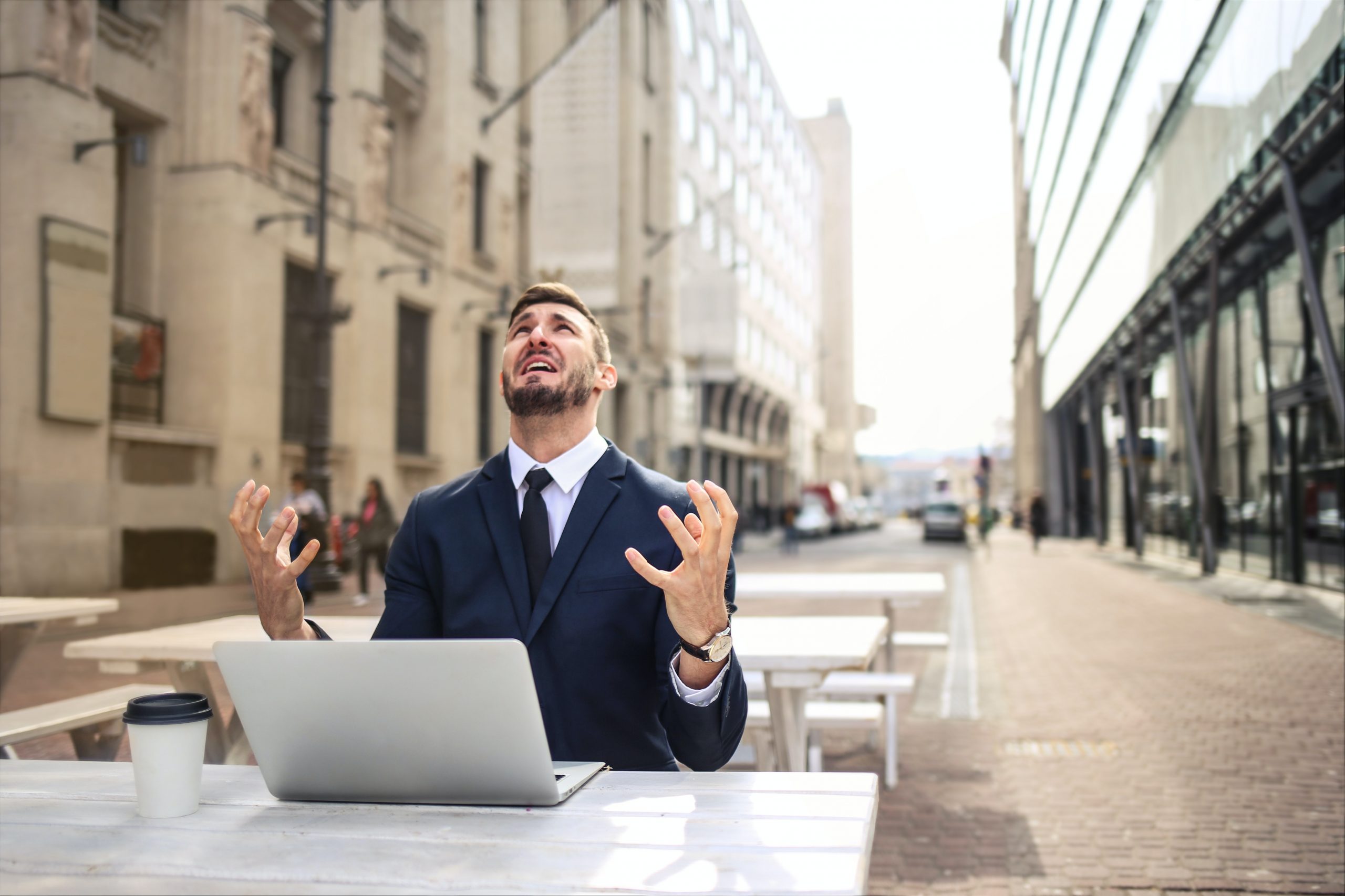 Um empresario com medo sentado em uma mesa na rua. com um notebook sobre a mesa.